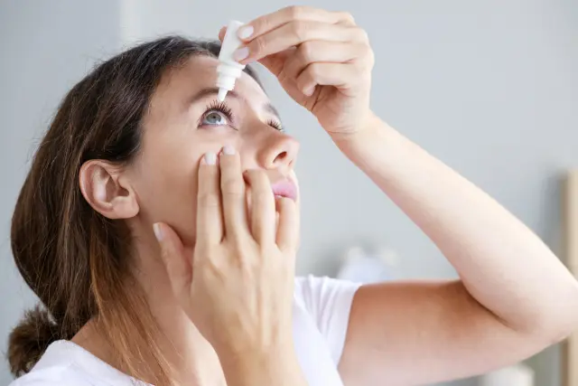 Mujer utiliza colirio en sus ojos.