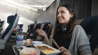 Mujer feliz viajando en avión y comiendo a bordo.