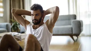 Un hombre joven realizando abdominales en su casa.