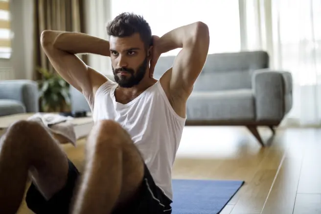 Un hombre joven realizando abdominales en su casa.