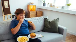 Un niño con sobrepeso comiendo hamburguesas y patatas fritas