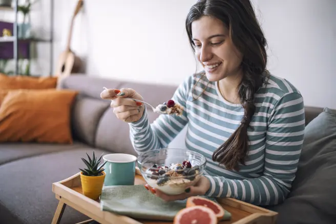 Una mujer desayuna un yogur griego con frutas en casa