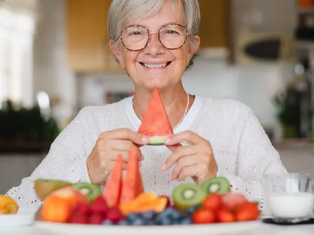 Una mujer mayor sostiene una porción de sandía mientras desayuna comida saludable.