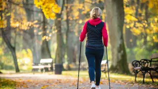 Una mujer practicando marcha nórdica en un parque de una ciudad.