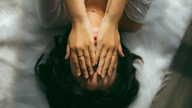Una mujer se tapa la cara con las manos en señal de cansancio.