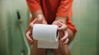Una mujer sentada en el váter sosteniendo un rollo de papel higiénico.
